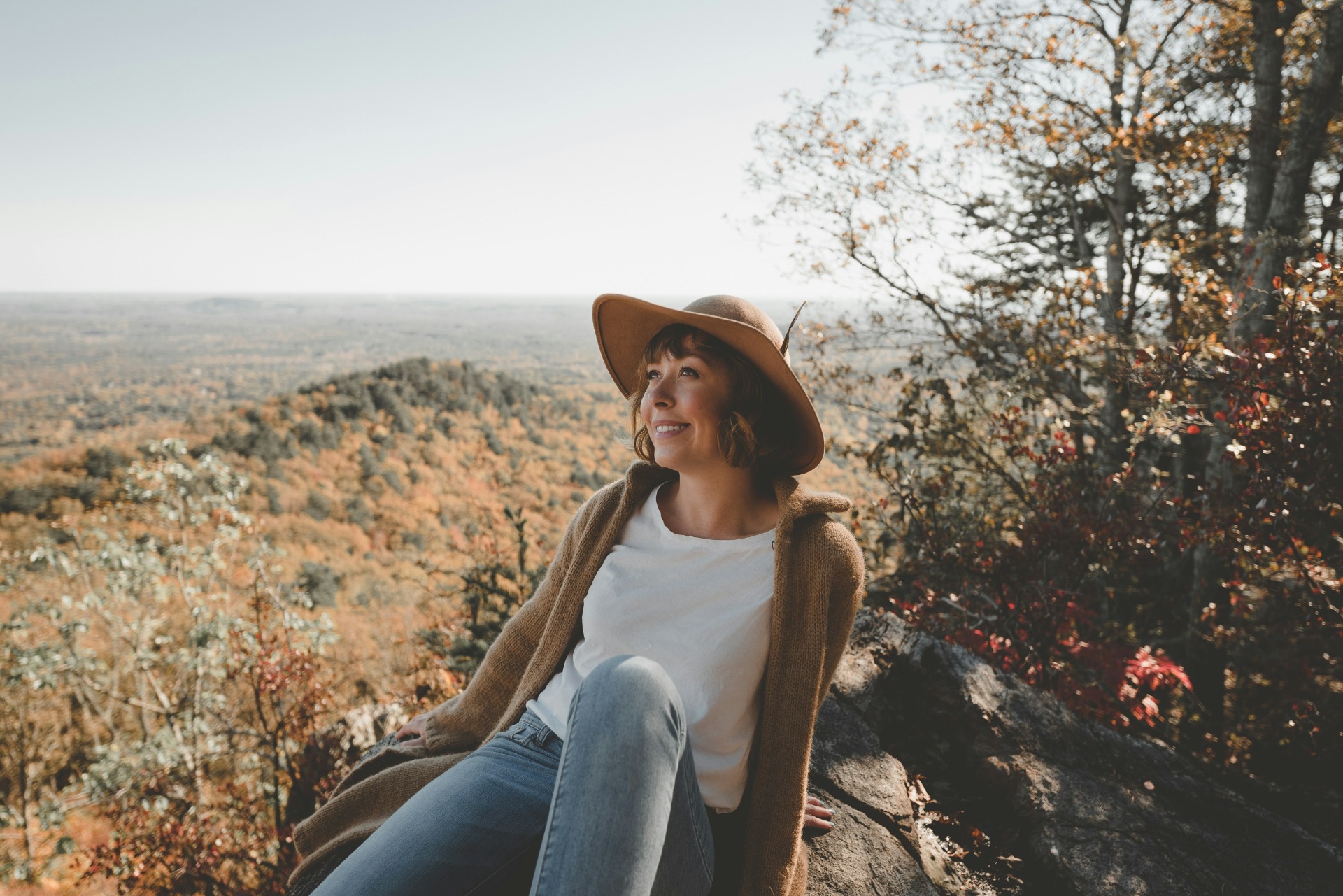 Woman in a wide-brim hat sitting on a mountain overlook, taking in autumn views — a moment of calm during the perimenopause and menopause transition
